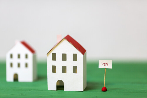 miniature-house-model-near-sale-tag-green-textured-desk-against-white-backdrop.jpeg